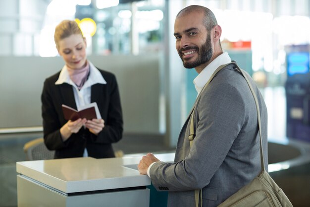 Viajero sonriente de pie en el mostrador mientras el asistente revisa su pasaporte