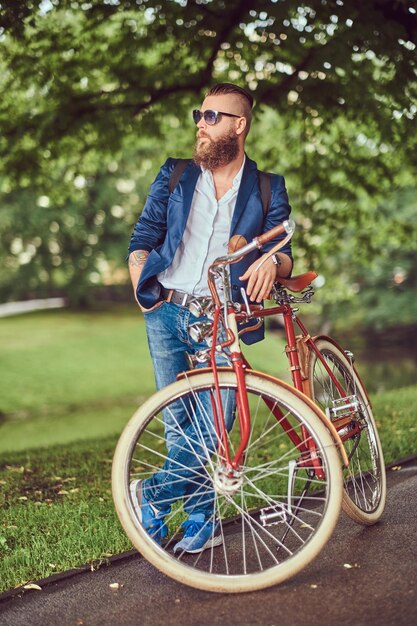 Un viajero vestido con ropa informal y gafas de sol con una mochila, relajándose en un parque de la ciudad después de andar en bicicleta retro.