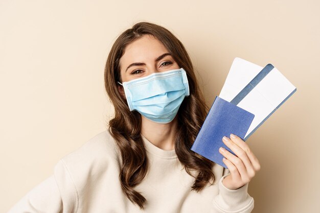 Viajes y pandemia de covid cierran el retrato de una mujer sonriente con una máscara médica que muestra el pasaporte con el...