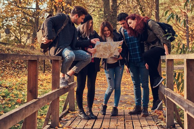 Viajes, senderismo, concepto de aventura. Grupo de jóvenes amigos caminando en el bosque colorido de otoño, mirando el mapa y planeando una caminata.