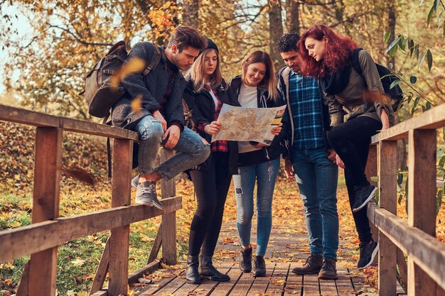 Viajes, senderismo, concepto de aventura. Grupo de jóvenes amigos caminando en el bosque colorido de otoño, mirando el mapa y planeando una caminata.