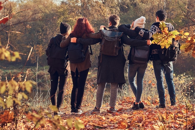 Viajes, senderismo, concepto de aventura. Vista trasera de jóvenes amigos abrazándose y mirando el lago en un hermoso bosque de otoño.