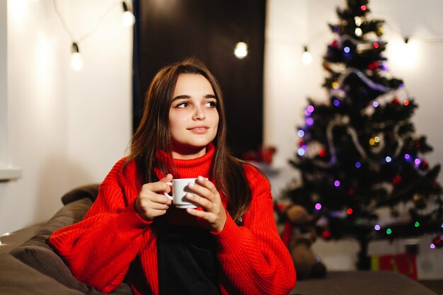 Vibes de navidad y año nuevo. Decoraciones para el hogar. Encantadora joven en suéter rojo