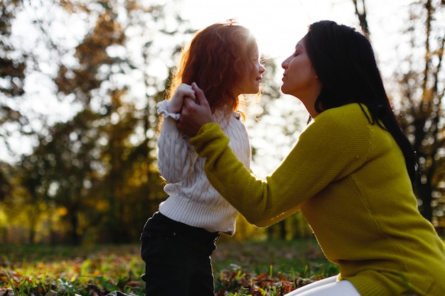 Vibraciones otoñales, retrato de familia. La encantadora mamá y su hija pelirroja se divierten sentadas en el caído