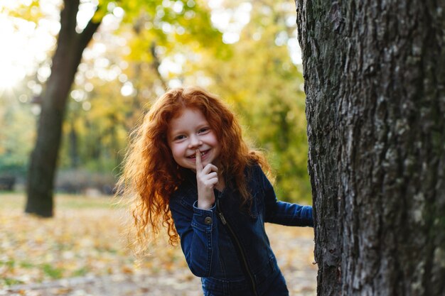 Vibraciones otoñales, retrato infantil. Encantadora y roja niña de pelo se ve feliz caminando y jugando en t