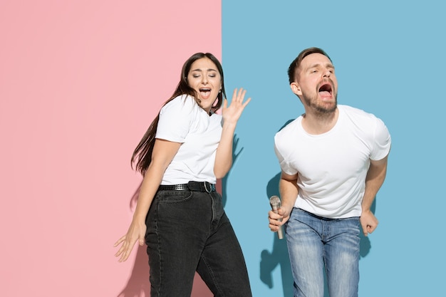 Vibras. Bailar, cantar, divertirme. Hombre y mujer joven y feliz en ropa casual en pared bicolor rosa, azul. Concepto de emociones humanas, expresión facial, relaciones, anuncio. Hermosa pareja.