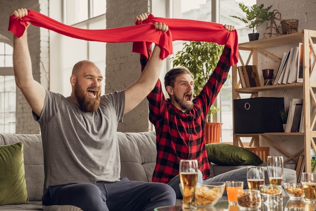 Foto gratuita victoria. amigos emocionados y felices viendo baloncesto, fútbol, fútbol, partido de tenis, campeonato en el sofá de casa. fans emocionados animando a su equipo nacional favorito. deporte, tv, diversión.