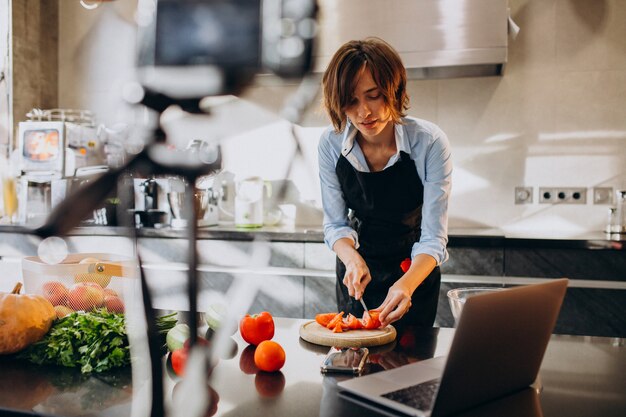 Foto gratuita videoblogger joven cocinando en la cocina y filmando