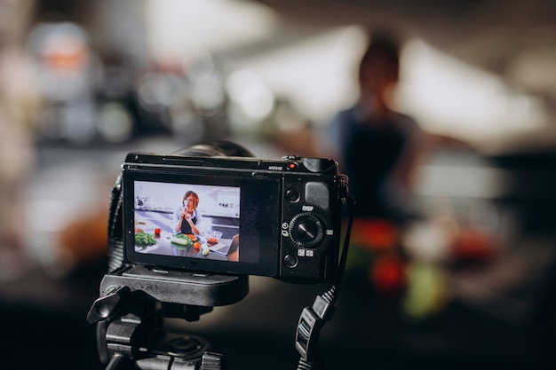 Foto gratuita videoblogger joven cocinando en la cocina y filmando