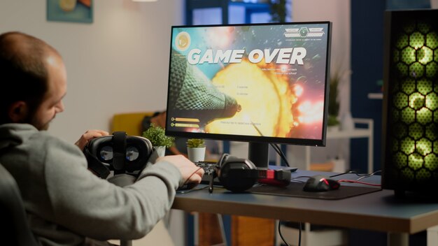 Videojugador que pierde gráficos ciberespacio videojuego sentado en una silla de juego usando un controlador inalámbrico y auriculares VR jugando en una computadora potente. Triste pro cyber man campeonato en línea de transmisión