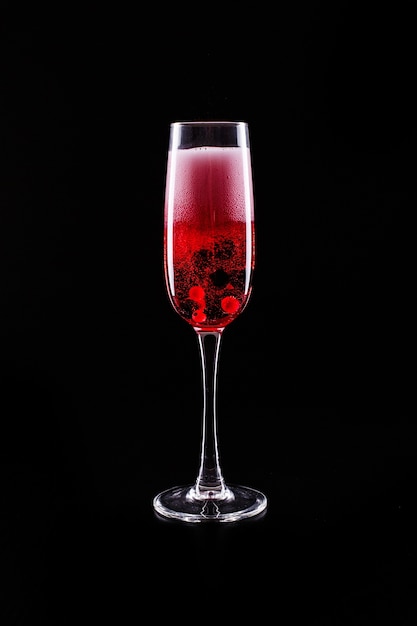 El vidrio con las bayas y el cóctel rojo del alcohol del champán se coloca en fondo negro