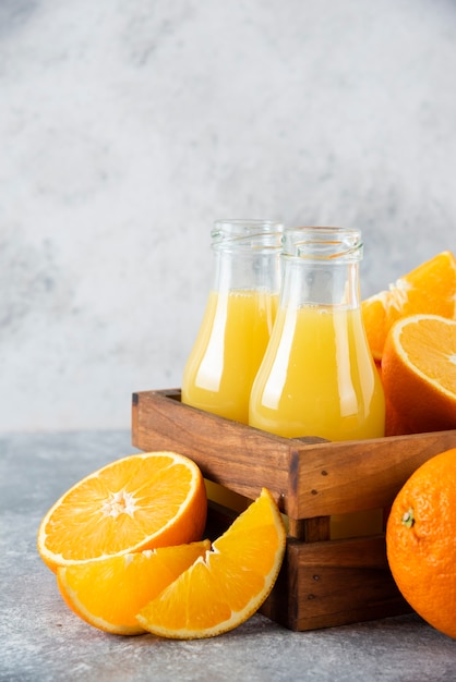 Una vieja caja de madera llena de frutas naranjas y jarras de jugo de vidrio en la mesa de piedra.