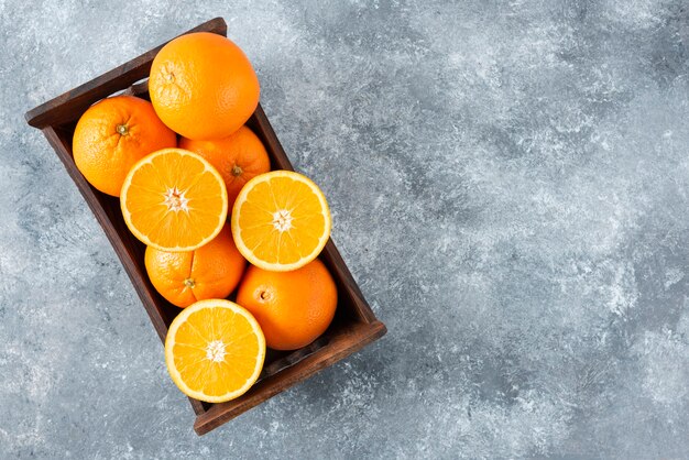 Una vieja caja de madera llena de jugosas frutas naranjas en rodajas y enteras.