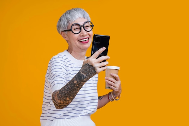 Foto gratuita vieja mujer asiática tatuada usando un teléfono inteligente decir hola saludo conversación videollamada a su amiga conversación casual mujer mayor de asia usando un dispositivo de teléfono inteligente tecnología de aplicación de fácil conexión
