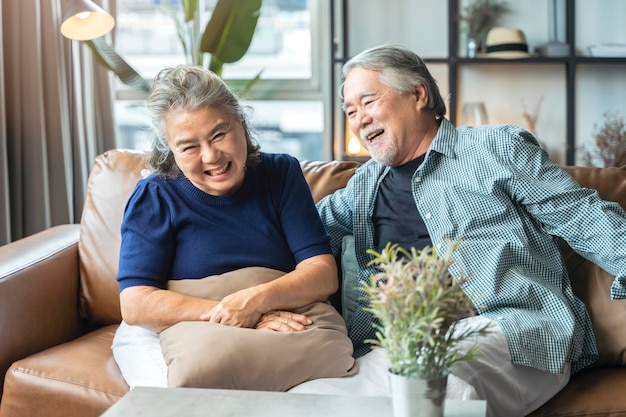 La vieja pareja de jubilados asiáticos disfruta de conversar juntos en el sofá con felicidad, risa, sonrisa y alegría en el concepto de período de cuarentena en casa.