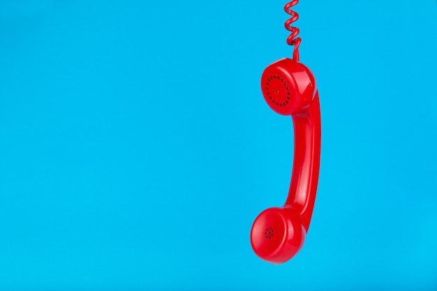 Viejo auricular de teléfono rojo colgando sobre una superficie azul