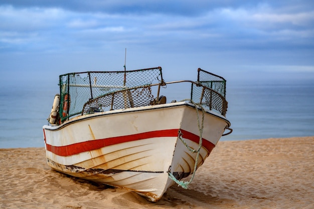 Viejo barco pesquero oxidado en la arena de la playa con una vista del paisaje marino detrás