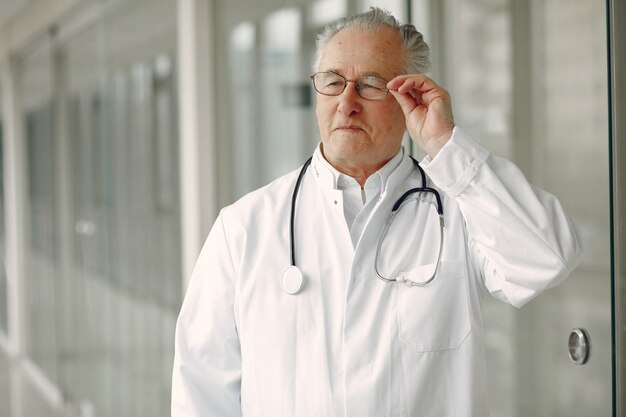 Viejo doctor en uniforme de pie en el pasillo