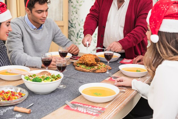 Viejo hombre cortando pollo al horno en la mesa de Navidad