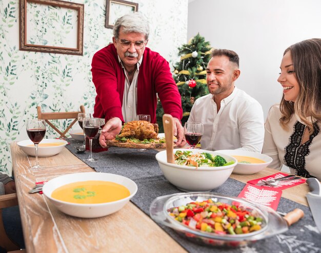 Viejo hombre poniendo pollo al horno en la mesa de Navidad