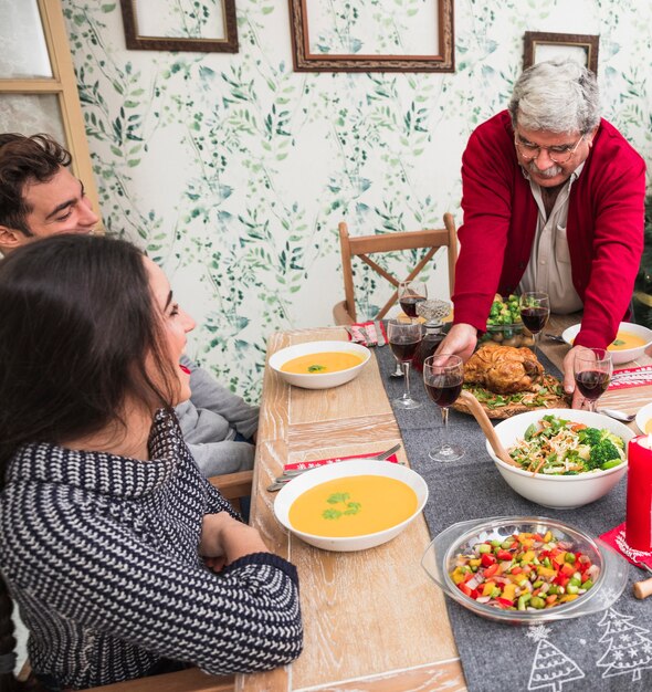 Viejo hombre poniendo pollo asado en mesa festiva