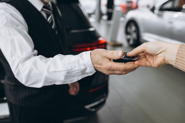 Viejo hombre que recibe las llaves del automóvil en una sala de exposición de automóviles