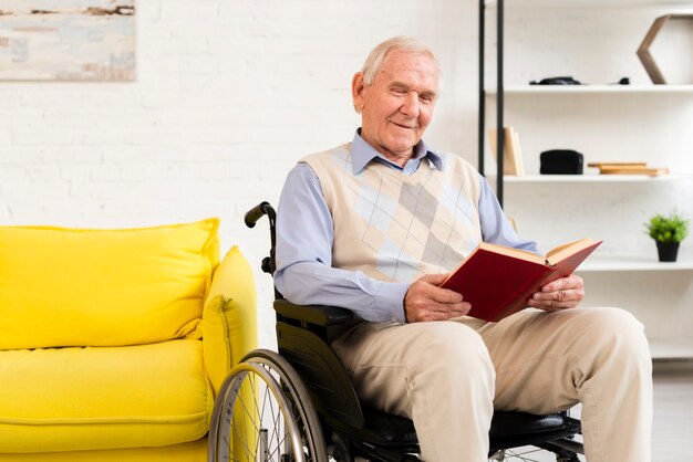 Viejo hombre sentado en silla de ruedas mientras lee el libro