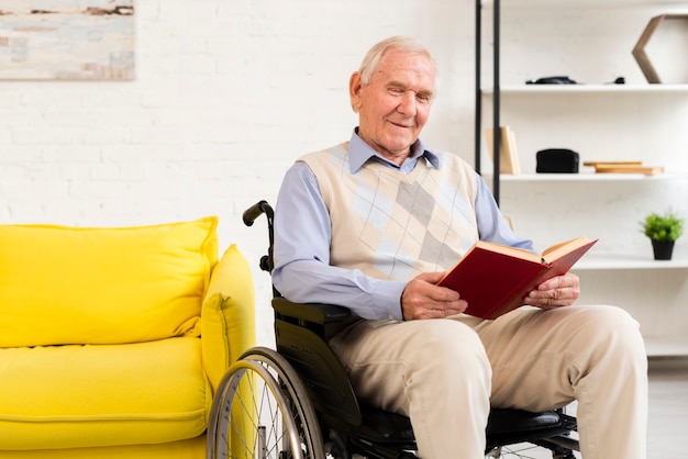 Viejo hombre sentado en silla de ruedas mientras lee el libro