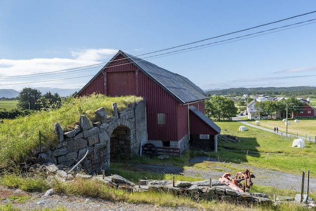 Viejo puente de piedra que conecta a un granero rojo rodeado de vegetación y árboles cortos en Alesund, Noruega