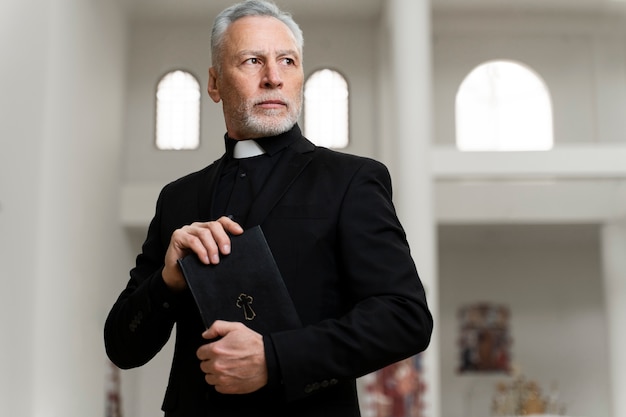 Foto gratuita viejo sacerdote de tiro medio sosteniendo la biblia