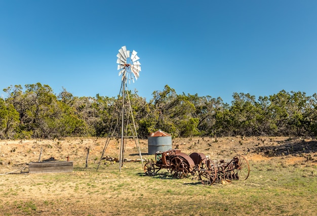 Viejo tractor oxidado y un molino de viento en las carreteras secundarias de Texas