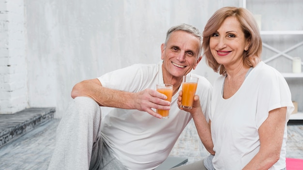 Viejos pares felices que se sientan en casa que sostienen el vidrio de jugo