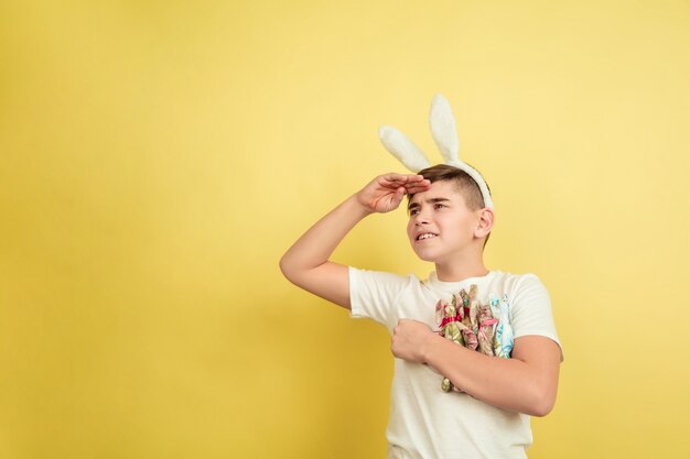 Viendo hacia adelante. Decorar. Muchacho caucásico como un conejito de Pascua sobre fondo amarillo. Felices saludos de pascua. Hermoso modelo masculino. Concepto de emociones humanas, expresión facial, vacaciones. Copyspace.