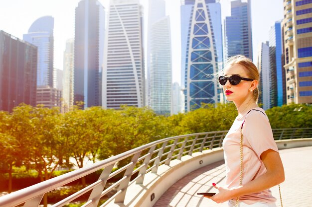 El viento sopla el pelo de la mujer mientras que ella se coloca en el puente antes de los rascacielos hermosos de Dubai