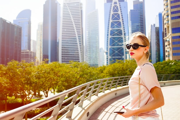 El viento sopla el pelo de la mujer mientras que ella se coloca en el puente antes de los rascacielos hermosos de Dubai