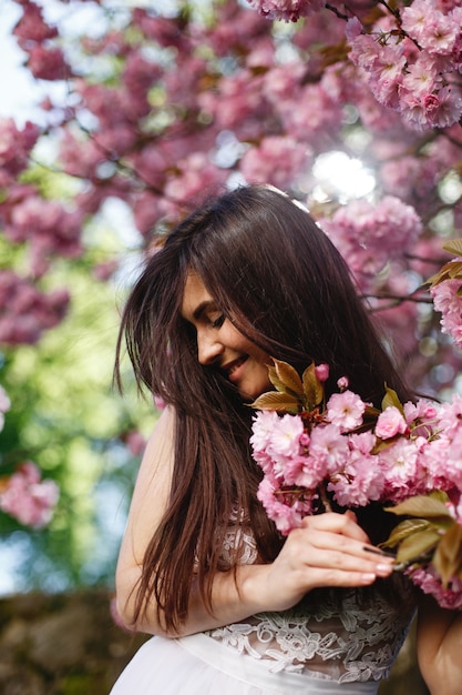 El viento sopla el pelo de la mujer morena mientras ella posa ante un árbol floreciente de sakura