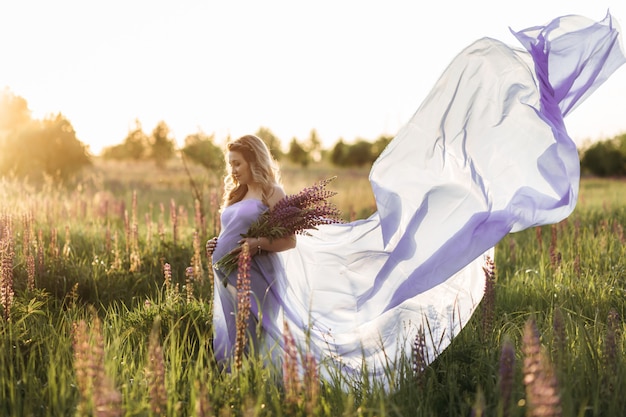 El viento sopla el vestido violeta de una mujer embarazada mientras ella se para en el campo de la lavanda