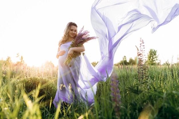 El viento sopla el vestido violeta de una mujer embarazada mientras ella se para en el campo de la lavanda