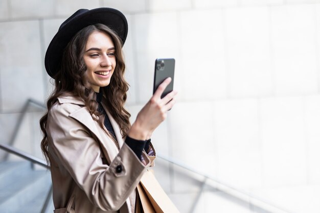 Viernes negro, mujer con smartphone y sosteniendo la bolsa de compras mientras está de pie en la pared del centro comercial