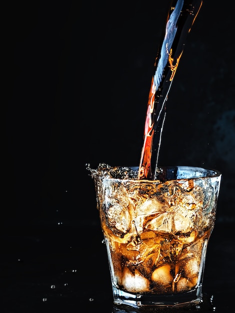 Se vierte refresco de cola suave carbonatado en un vaso de hielo.