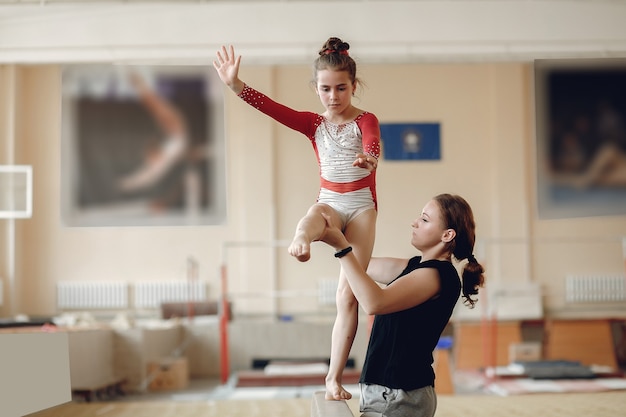 Viga de equilibrio de gimnasia infantil. Atleta gimnasta chica durante una barra horizontal de ejercicio en competiciones de gimnasia. Entrenador con niño.