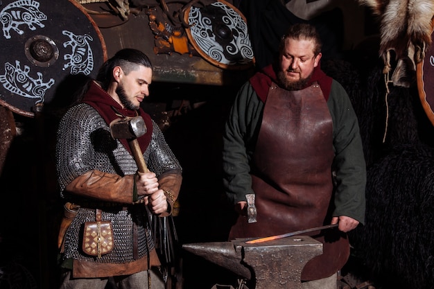 Viking forja armas y espadas en la herrería. Un hombre con ropa de guerrero está en la herrería.