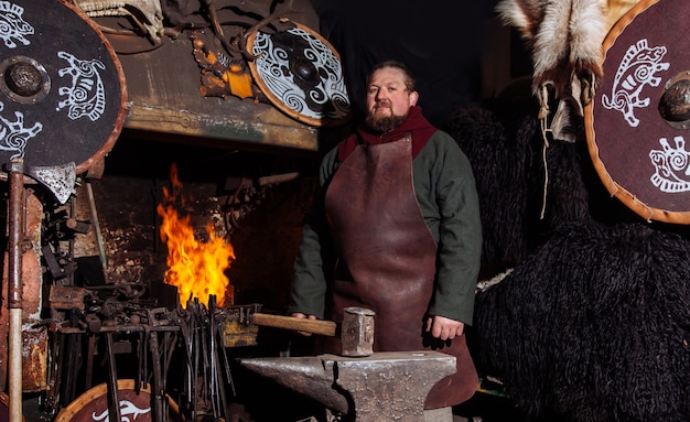 Viking forja armas y espadas en la herrería. Un hombre con ropa de guerrero está en la herrería.