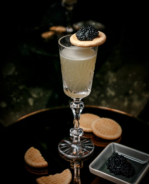 vino blanco en copa de cristal servido con caviar negro y galletas