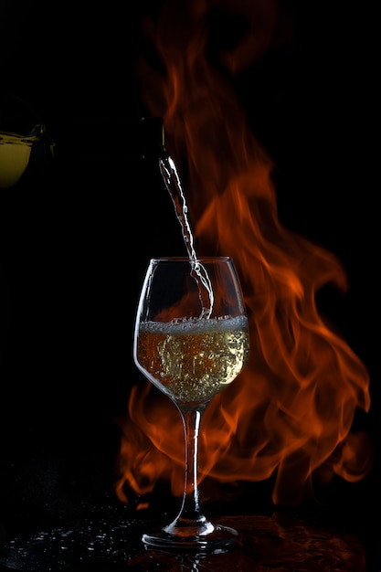el vino blanco se vierte en un vaso con tallo largo en un fondo oscuro con fuego