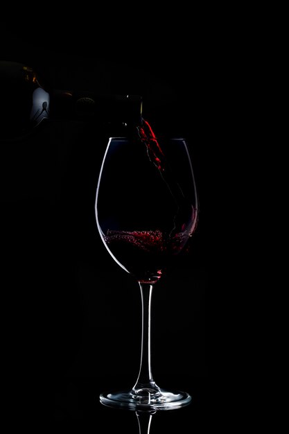 el vino tinto se vierte en un vaso con tallo largo en la oscuridad