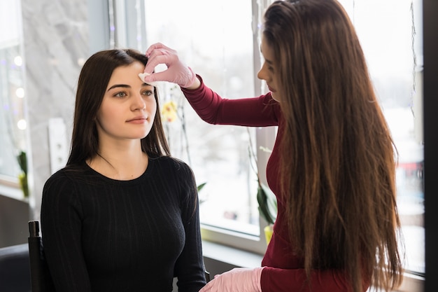 Visagiste hábil haciendo maquillaje de cejas para una chica con suéter negro