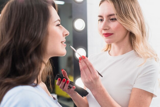 Visagiste haciendo maquillaje de labios al cliente.