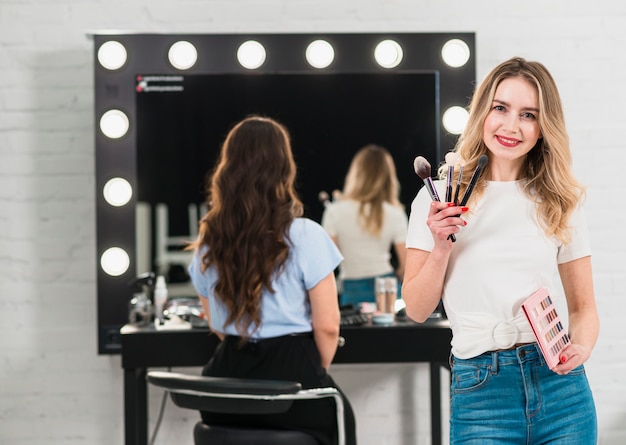 Visagiste con pinceles de maquillaje y paleta de sombras de ojos.