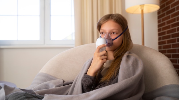 Vista de una adolescente que usa nebulizador en casa por problemas de salud respiratoria